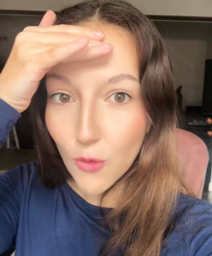 Une femme face à la caméra, une main posée sur le front.